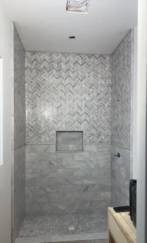 Shower with grey marble chevron mosaic above a marble tile wainscot, a recessed niche and a hexagon mosaic floor