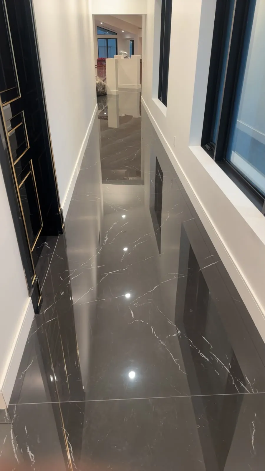 Long hallway with a polished dark marble-look tile floor reflecting the walls and a black door