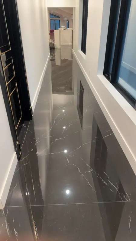 Long hallway with a polished dark marble-look tile floor reflecting the walls and a black door