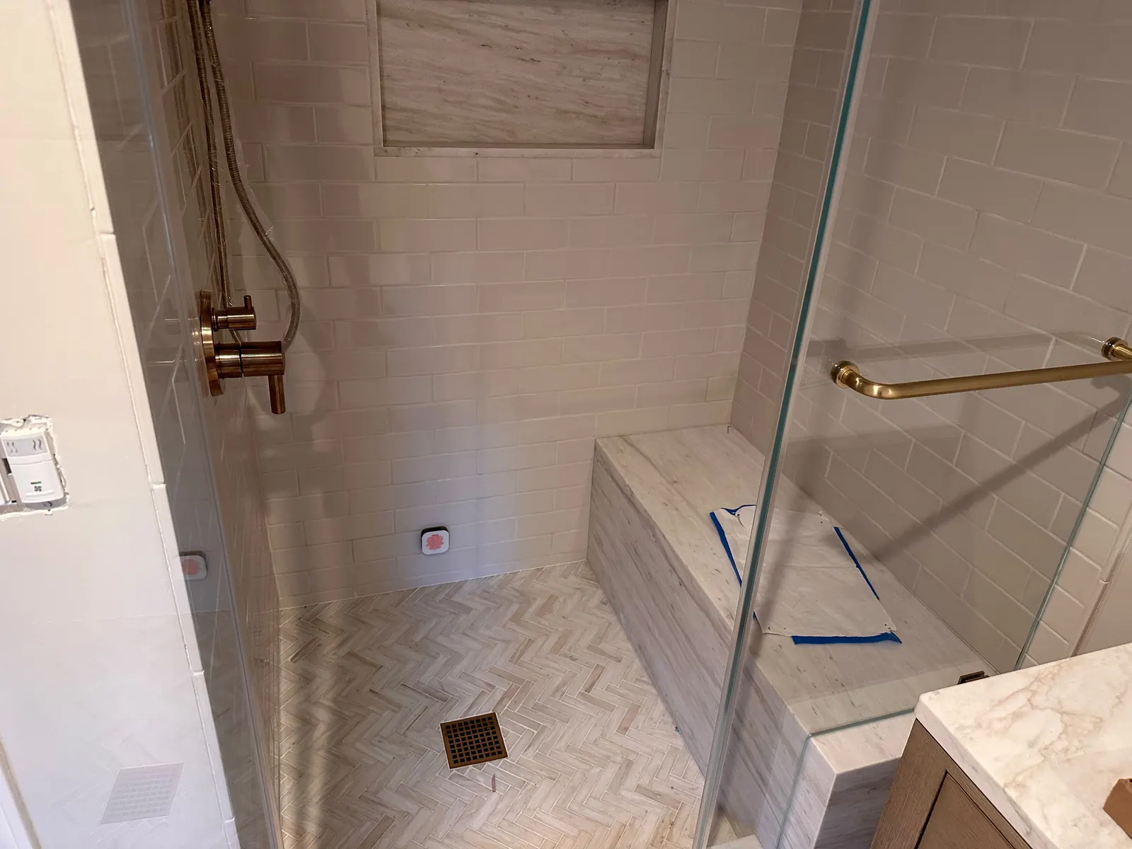 Walk-in shower with white subway tile, a stone bench, a long niche and a herringbone stone floor