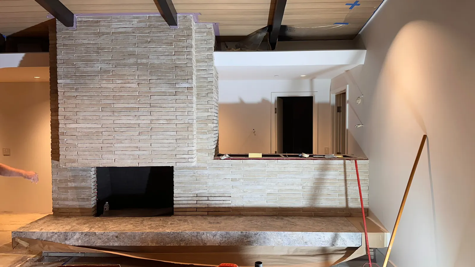 Fireplace wall during the job: brick-look tile wrapping the firebox and a ledge, with a stone hearth